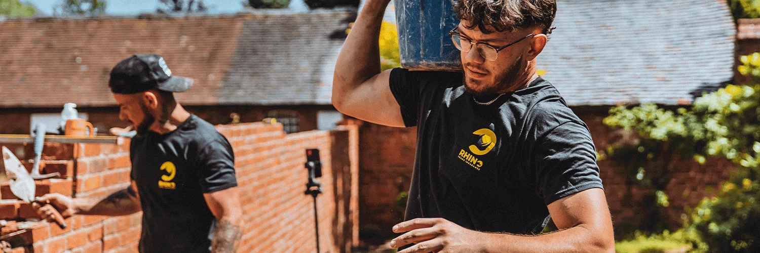 builders working on brick wall and carrying bucket on site