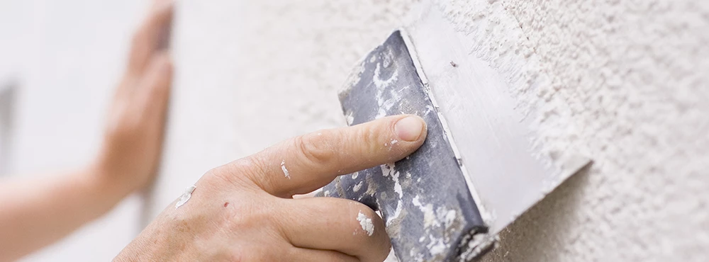 roughcaster scraping off rough surface on wall